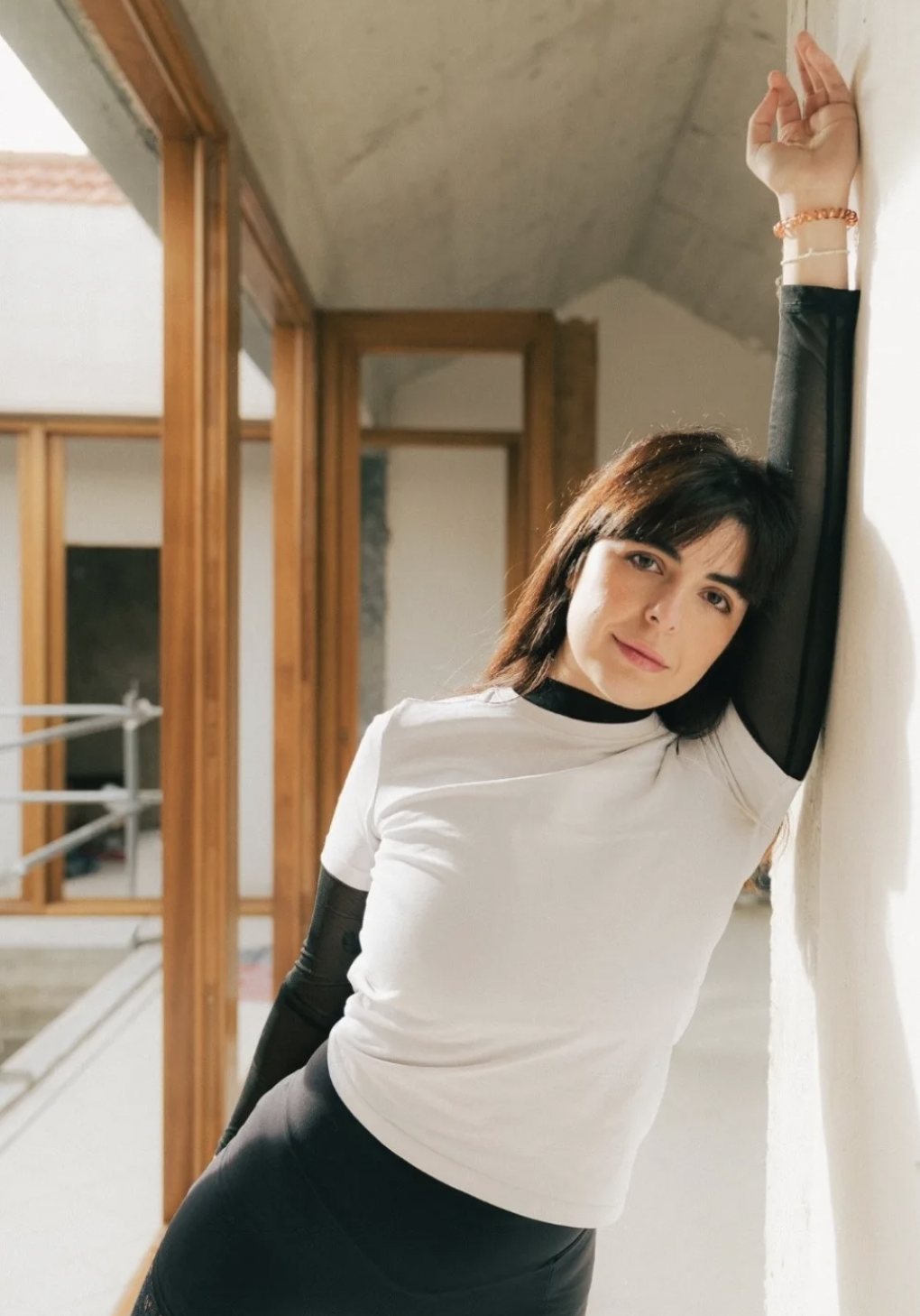 Clara deMin leaning against a white wall with one arm raised