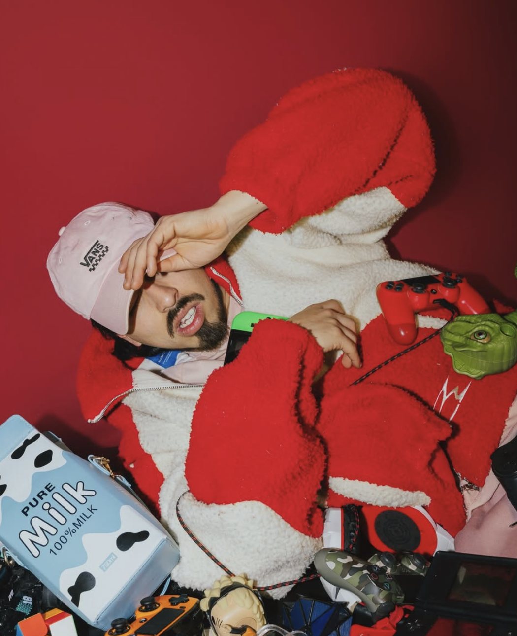 Gelatte in a red and white fleece jacket and pink cap, surrounded by game controllers and toys